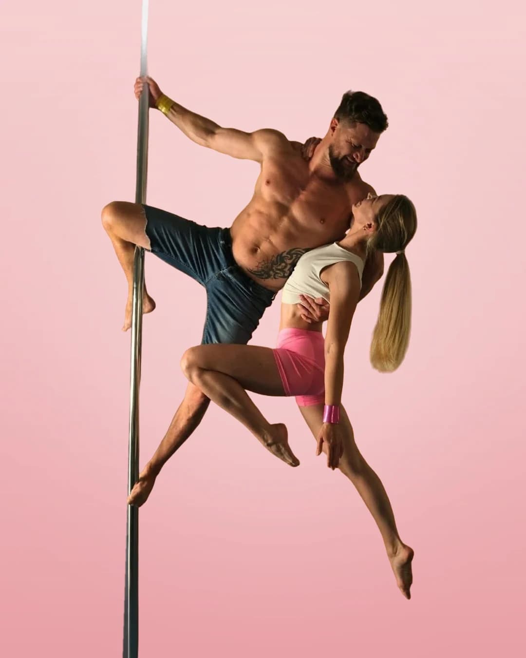 Two pole dancers in a duo pose on the pole, wearing SneakyDeez wrist wraps