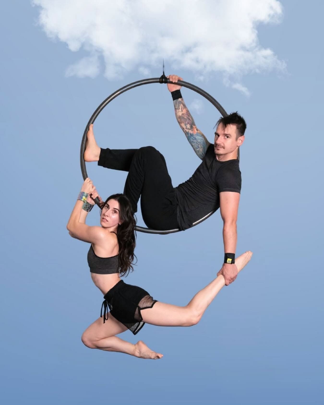 Two aerialists on an aerial hoop against a blue sky, wearing SneakyDeez wrist wraps