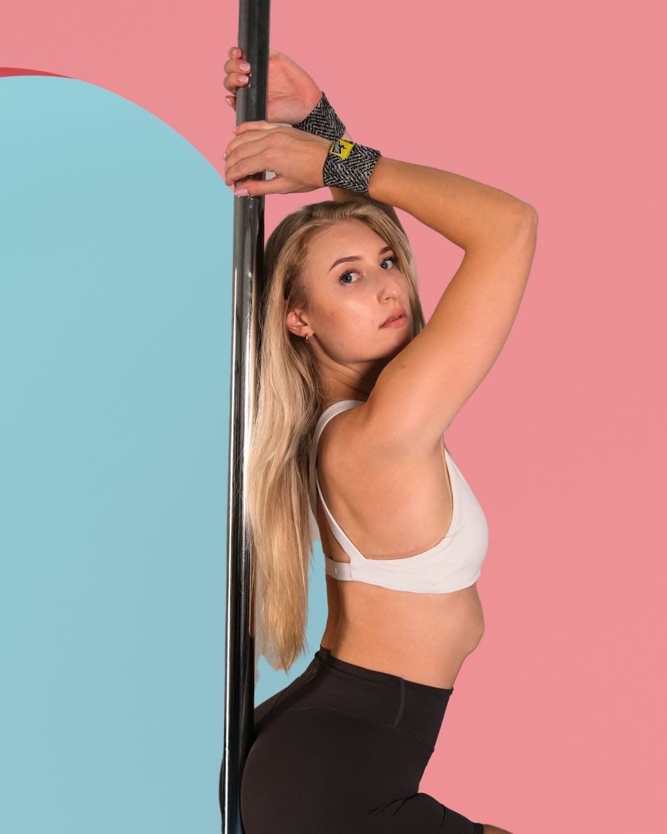 Pole dancer wearing SneakyDeez wrist wraps against a blush and powder-blue backdrop