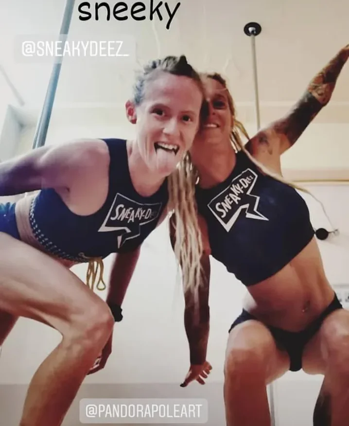 Two pole dancers in SneakyDeez crop tops and shorts pulling faces at the camera in a pole studio