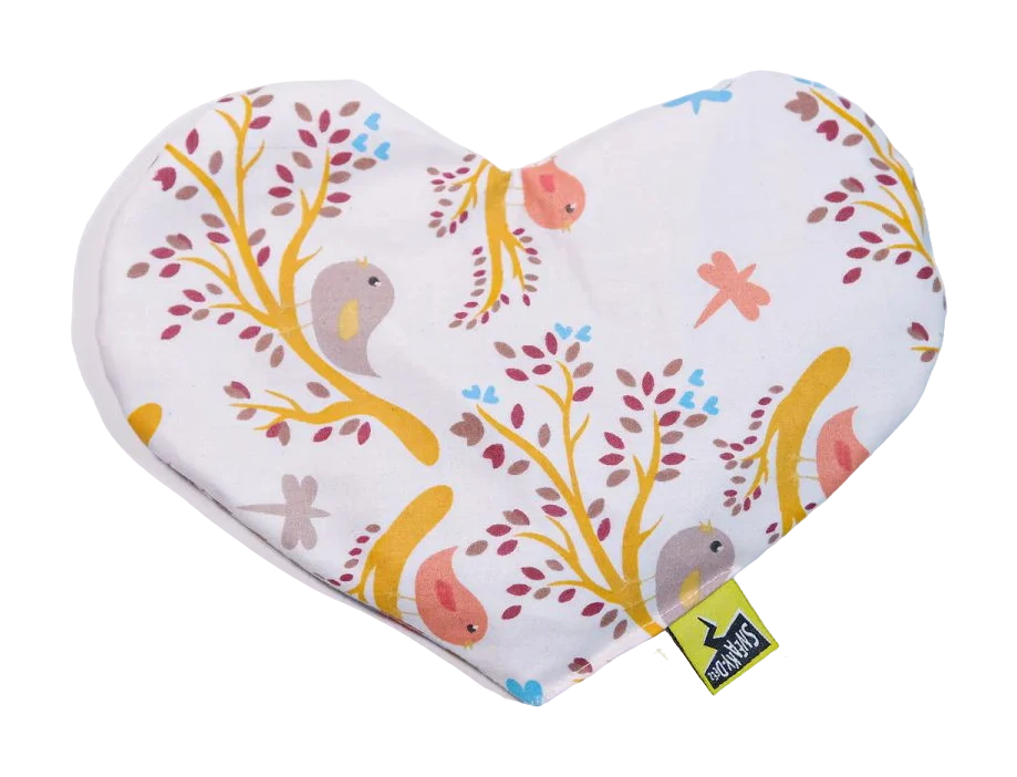 Heart-shaped fabric heat pack printed with birds, branches and dragonflies on a cream background, with a small yellow SneakyDeez label